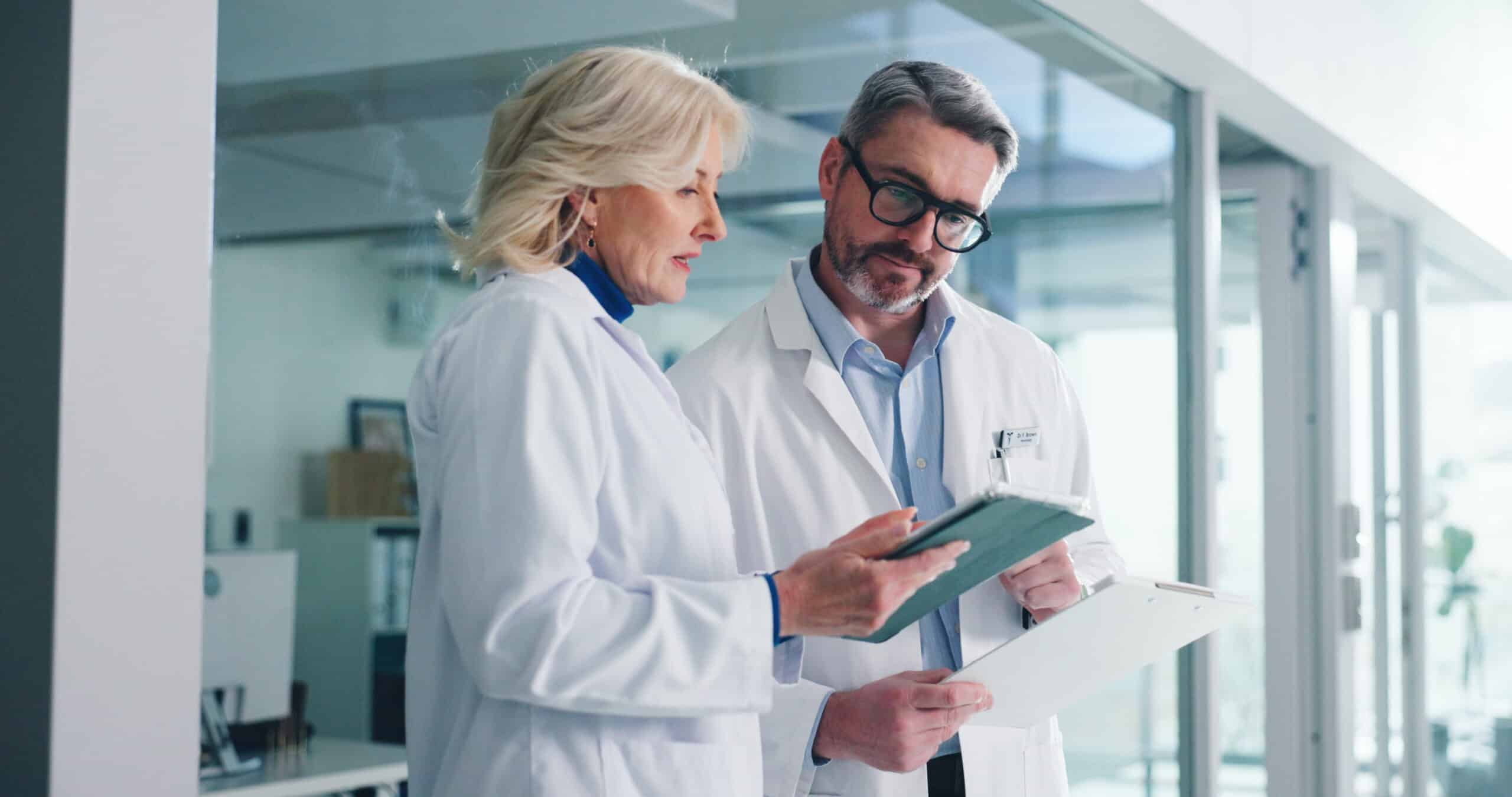 Two scientists in white lab coats discuss a tablet in a bright, modern laboratory.
